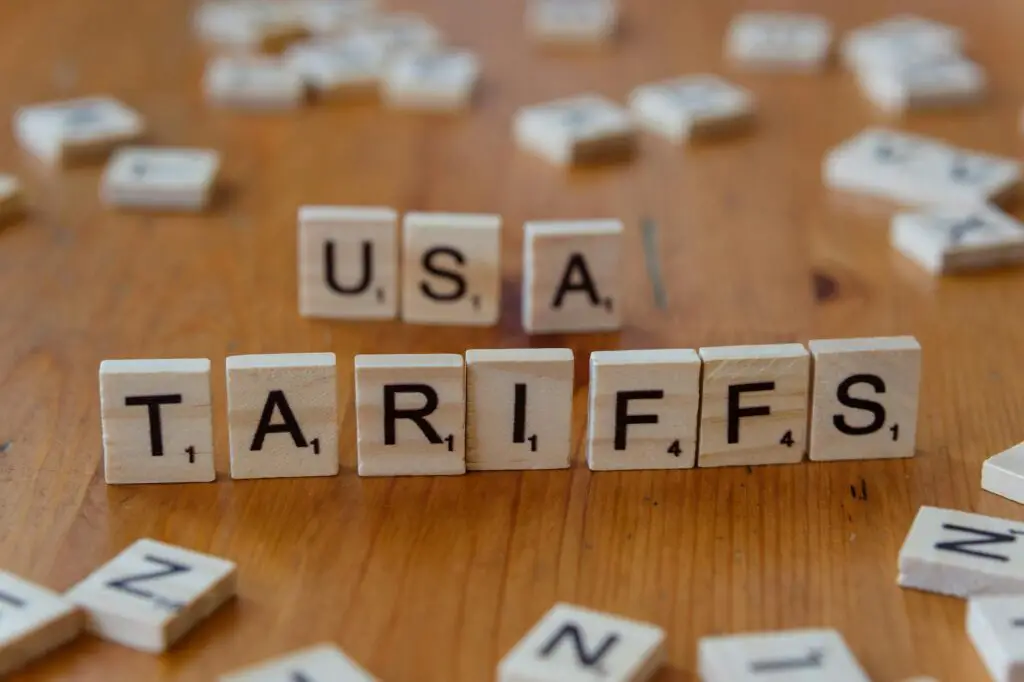 Wooden tiles spelling 'USA' and 'TARIFFS' on a wooden surface symbolizing trade issues.